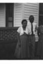Three unidentified people stand in front of a house.