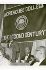 View of man standing at a podium. Banner in background reads, Morehouse College, 'The Second Century' .