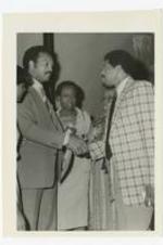View of Jesse Jackson shaking hands with a man, view of women in background.