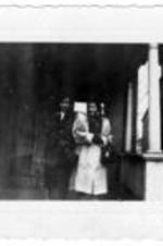 Two unidentified women in coats stand on a front porch.