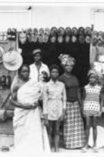 A group of people stand in front of a shop that sells hats, purses, shoes, and other accessories.