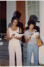 Two unidentified women record notes outside of a building.