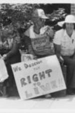 Three women are shown sitting, with one of them holding a protest sign that reads "We Deserve The Right To Live!!" The women were marching in Eufaula, Alabama to protest the killing of the Russaw brothers by police.