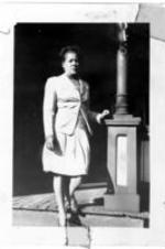 An unidentified woman stands on a house porch.