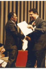 Joseph E. Lowery greets Maynard Jackson during an unknown event. Evelyn G. Lowery and Karen Lowery sit in the background.