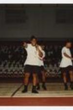 A group of young women, wearing matching outfits, stand on the basketball court at a homecoming step show.