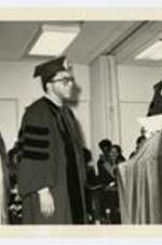 President Elias Blake Jr. stands at the podium, while two other men look on, at commencement.