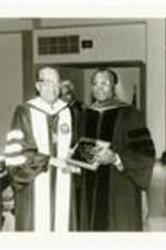 Written on verso: President Hugh M. Gloster presents 25-year plaque to Dr. Tobe Johnson, Chairman of the Department of Political Science. He became Chairman in 1983. Commencement - May 22, 1983.