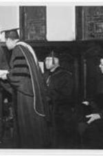 Dr. Harry Richardson awards a man a diploma and shakes his hand during commencement.