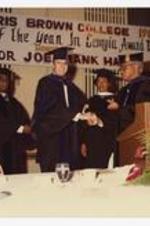 Indoor view of men shaking hands at podium, on sign "Morris Brown College 1983....Man of the Year in Georiga Award Dinner Honoring Governor Joe Frank Harris".