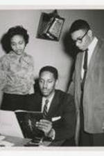 A woman and two men look at a booklet. Written on verso: Class Room Pictures, Mary Mina Moore, Rev. Roland E. Haynes, Bobby McClain, Photo by Tracy O'Neal.