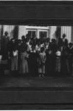 View of an unidentified group of men and women standing outside of a building.