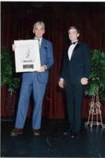 Two unidentified men stand on stage, one holding an award at the Atlanta Student Movement 20th anniversary event.