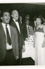 Hugh Morris Glouster sing with his wife and others, view of cake in background.