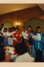 A group of young women are shown holding candles and reading from a paper during a SCLC/W.O.M.E.N. Bridging the Gap: Girls to Women Mentoring Program event.