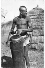 An African man playing a tam-tam drum.