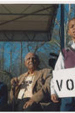 A young boy holds a sign that says "VOTE" at the Selma Bridge Crossing Jubilee event. Evelyn and Joseph Lowery, seated, look on.