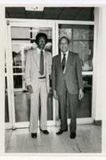 President Hugh Gloster standing with Arthur Ashe in front of a building.