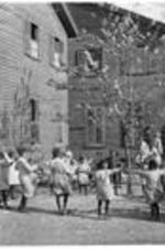 A group of children play around a tree ouside the home.