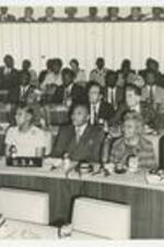 Edward A. Jones and others sit at a long table with with microphones. The sign on the table reads U.S.A.