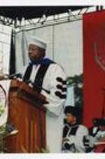 Hank Aaron, wearing a graduation cap and gown, stands at the podium at commencement.