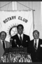 View of Maynard Jackson at a podium with members of the Atlanta Rotary Club.