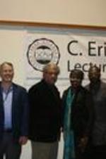 A group of Clark Atlanta University professors pose in front of the lecture series banner.