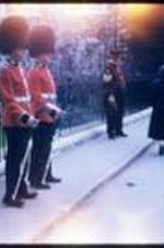 Two Queen's Guards and a yeoman warder stand outside a gate.