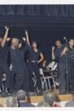 Men and women, wearing black shirts and pants, perform on stage at convocation.