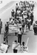 Demonstrators are shown walking down a street in a march prompted by the killing of the Russaw brothers in Eufaula, Alabama. Several demonstrators hold a banner that reads "Concerned Ministers For Human Rights".