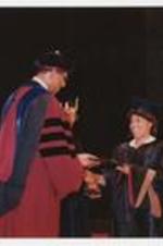 A woman receives her diploma and shakes hands with Thomas W. Cole, Jr. at a commencement.