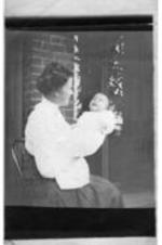 A woman sits on a porch holding a baby.