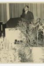 A man stands at a podium at the 75th Anniversary Band Concert.