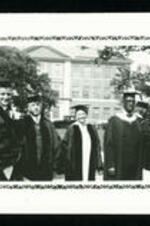 John Hope and two unidentified men and one women standing in front of building wearing academic regalia.