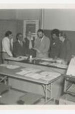Alfred Spriggs and a group of science professors read papers in a class room. Written on verso: CC, ca. 1970s, L to R (1-5), 1., 2. Alfred Spriggs, 3., 4., 5., Professors of Varying Science Departments.