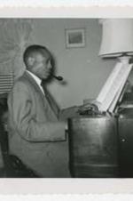 Edward A. Jones plays a piano organ with sheet music and pipe.