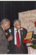 U.S. Representative John Conyers reads text from an award plaque that Joseph E. Lowery and an unidentified woman hold at the Stand Up &amp; Act Awards.