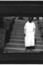 An unidentified woman stands on steps wearing a white dress.