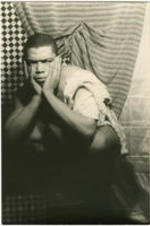 Portrait of Alvin Ailey crouching on a pedestal. Written on verso: Alvin Ailey; Photograph by Carl Van Vechten; 146 Central Park West; Cannot be reproduced without permission; March 22, 1955.