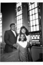 Rev. and Mrs. Rogers Randall and their daughter pose for a photo amongst the pews in a church. Written on verso: Rev &amp; Mrs. Rogers Randall and daughter. Rogers Randall Chestnut ST. Presbyterian church Wilmington, NC.