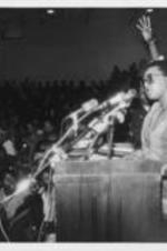 Billie Jean Young is shown addressing an audience of college students at the Pilgrimage to Washington kickoff rally in Tuskegee, Alabama. Written on verso: Southern Ru[r]al Women's Network director Ms. Billie Jean Young addresses audience at voting rights rally. Ms. Young played a organization played a large role in the SCLC pilgrimage to Washington.