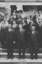 Men and women, part of faculty and staff of Morris Brown College, gather for a portrait outside of a campus building. Front center is president John H. Lewis.