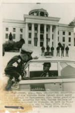 Alabama State Patrol troopers stand guard outside the capitol building in Montgomery, Alabama. Caption on photo reads: (MR1) MONTGOMERY, Ala., Mar. 18 -- CAPITOL SECURITY -- Troopers of the Alabama State Patrol stand guard at the capitol in Montgomery, Ala. today providing the tightest security for Gov. George Wallace of any Alabama governor in history. At left is Major Walter Allen. In the car is Capt. Billy Bishop.
