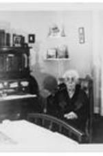 An unidentified elderly woman seated in a bedroom.