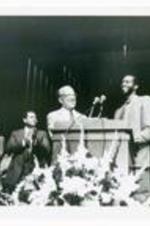President Hugh Gloster with unidentified persons on stage. Written on verso: Homecoming Assembly.