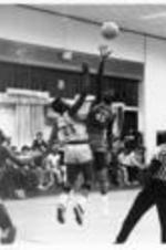 People watch two men jump for a basketball during a basketball game.