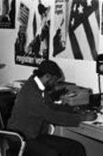 An unidentified man works at a desk in a VEP office filled with posters and copy equipment.