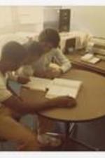 View of three students at table. Written on verso: "Alelva Swint tutors 2 freshman men in math 1982 (Fall)".