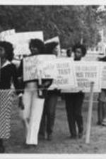 A group of Augusta College students and others are shown demonstrating with anti-apartheid signs to protest the performance of a South African boys choir at Augusta College. Written on verso: Pickits [sic]