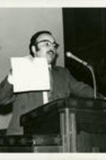 Portrait of Wiley Perdue speaking at a podium. Written on verso: Mr. Wiley A. Perdue, business manager.